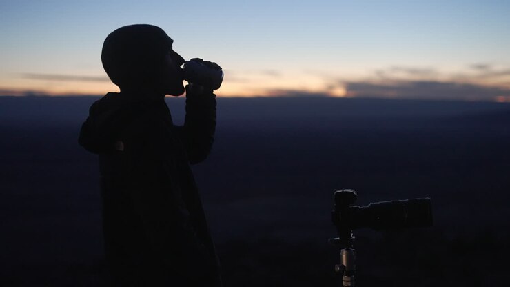 Young astro photographer takes photos after sunset while sipping on a beverage