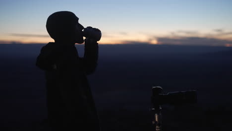 Der-Junge-Astrofotograf-Macht-Nach-Sonnenuntergang-Fotos,-Während-Er-An-Einem-Getränk-Nippt