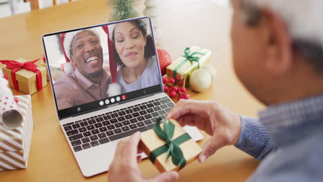 biracial man with gift having laptop video call with happy diverse couple