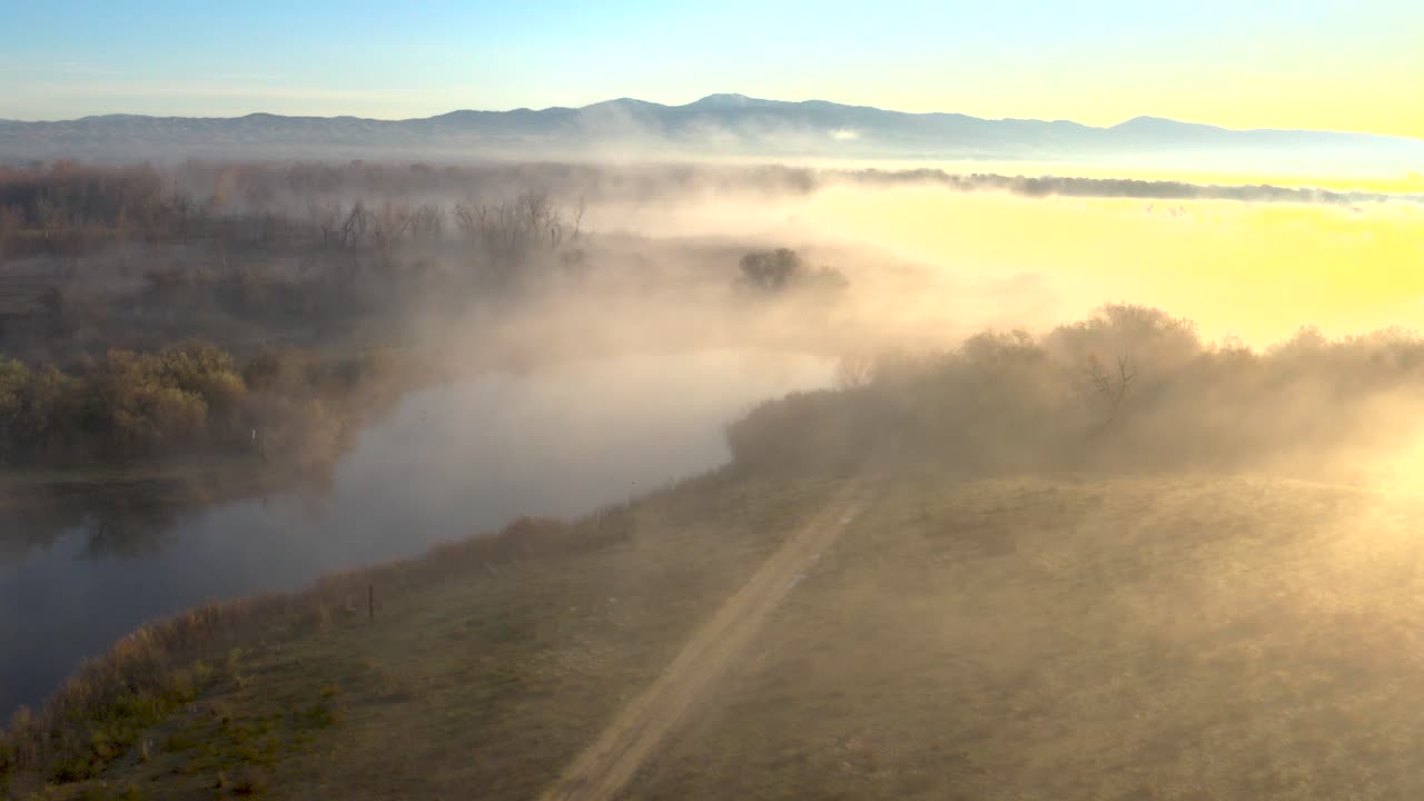 Aerial shot over a river in dense fog during a bright sunrise