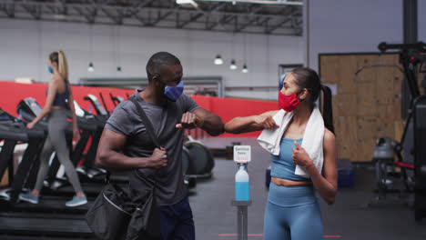 Fit-african-american-man-and-caucasian-woman-wearing-face-mask-greeting-each-other-by-touching-elbow