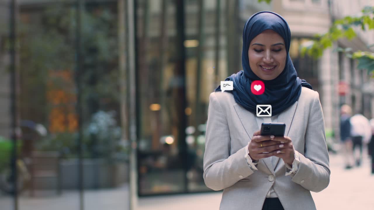 Smiling Muslim Businesswoman Standing Outside City Offices Looking At Mobile Phone With Motion Graphics Emojis Showing Multiple Networking Messaging And Social Media Notifications
