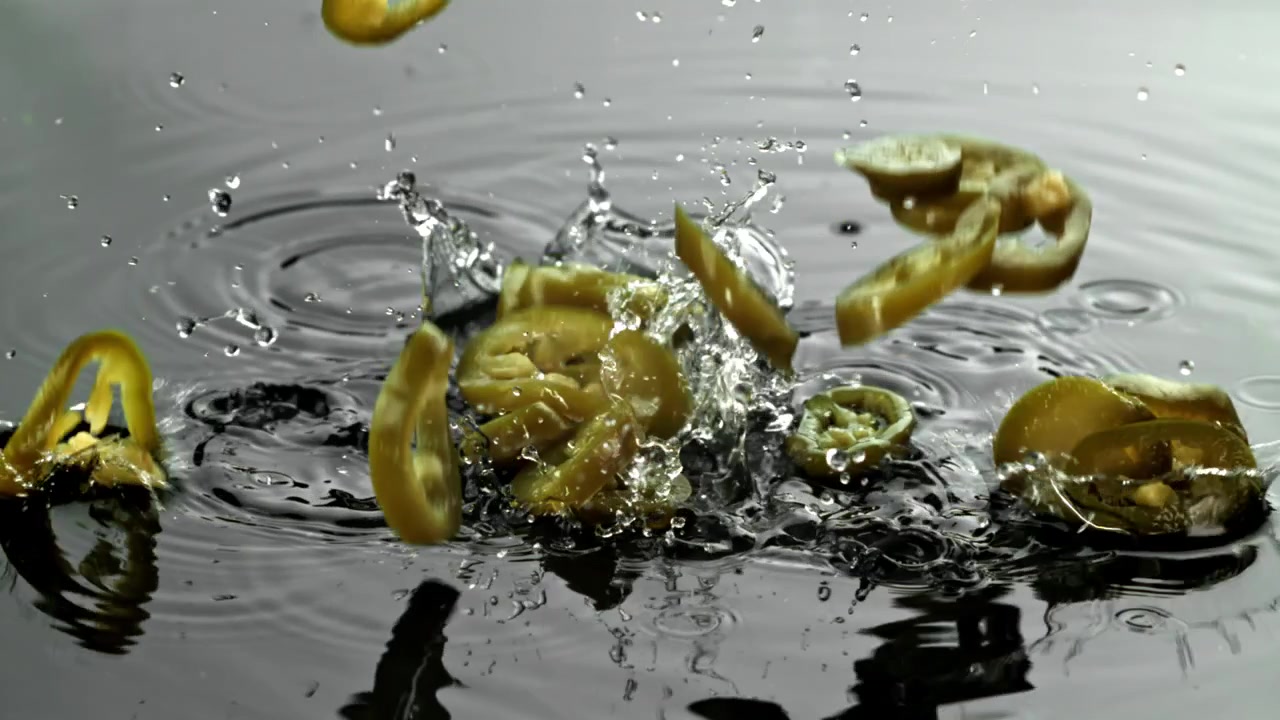Fette di jalapeño sottaceto che cadono nell'acqua al rallentatore
