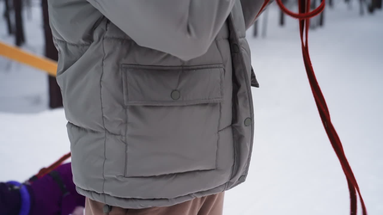 Young woman in gray winter jacket and knitted beanie looking off into distance in snowy forest, surrounded by pine trees during light snowfall, expressing peaceful, introspective, and cozy seasonal moment outdoors
