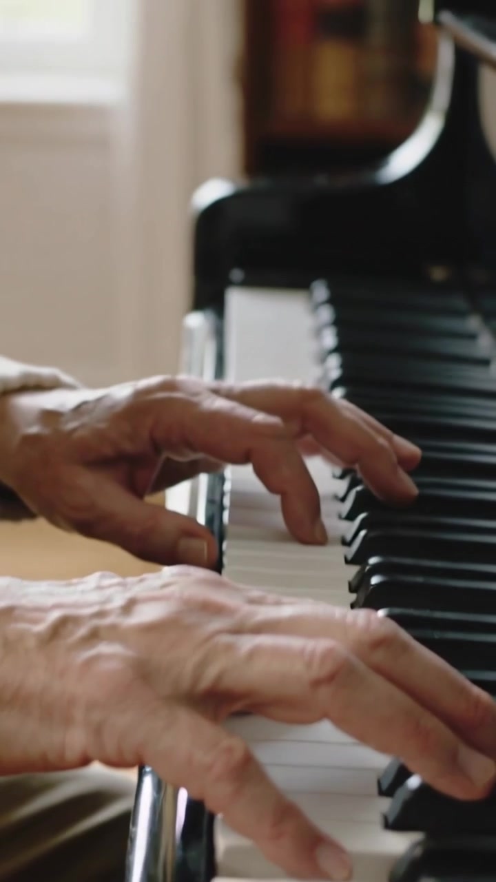 Vertical video: Playing senior pianist wearing glasses touching keys, practicing piece at home