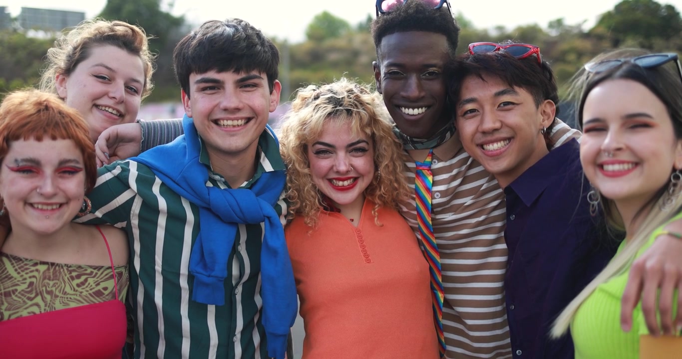Gruppo eterogeneo e felice di giovani amici sorridenti alla fotocamera all'aperto