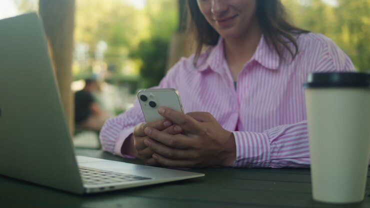 Donna che chatta con gli amici al telefono nel parco. Una studentessa è seduta all'aperto, beve caffè e comunica con lo smartphone.