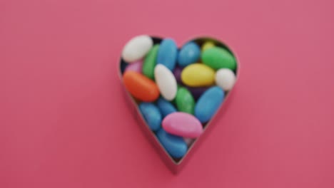 video of overhead view of multi coloured sweets in heart shape over red background