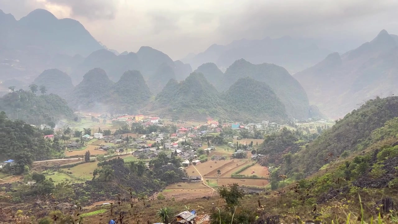 Cảnh quay lia thung lũng hiện ra ngôi làng, những cánh đồng nông nghiệp và những ngọn núi đá vôi xếp lớp trong không khí mờ sương với phong cảnh thiên nhiên và bầu trời mây nhẹ nhàng.