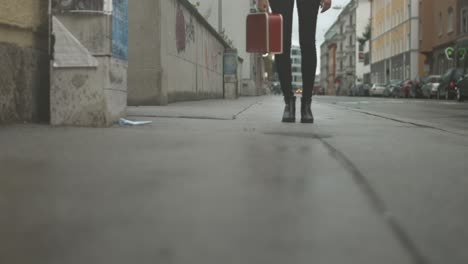 person walking with a red brief case towards the camera with city streets in the background on a rainy cloudy day