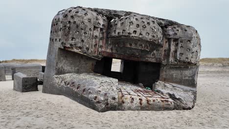a large, dilapidated section of a ww2 bunker with a gun porthole stands on the beach. europe denmark