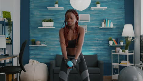 flexible woman with dark skin doing squat exercise using dumbbells