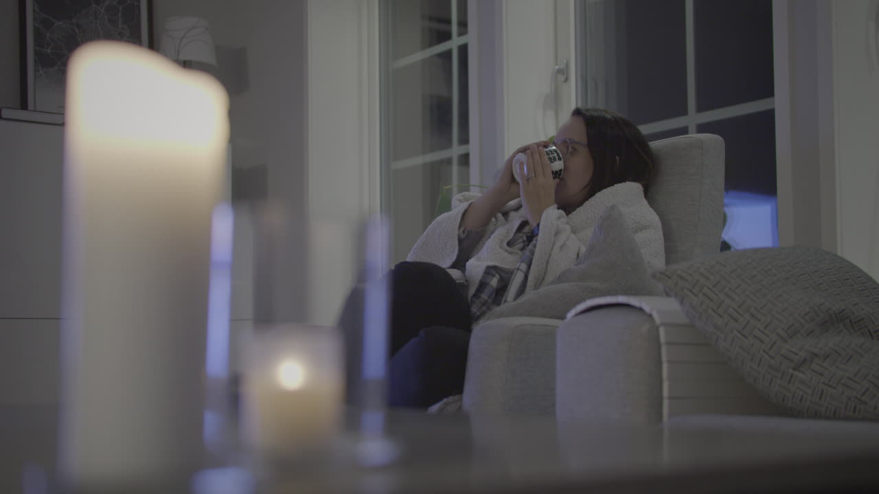 Donna attraente da sola a casa che si rilassa con una tazza di tè caldo e la TV di notte.