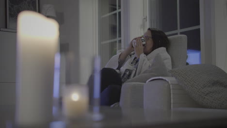 Attractive-Woman-alone-At-Home-Relaxing-With-Hot-Cup-of-Tea-And-TV-at-night