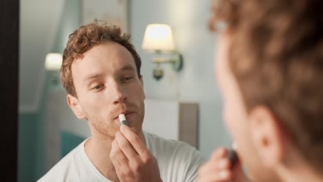 portrait in the mirror of a young man using hygienic lipstick