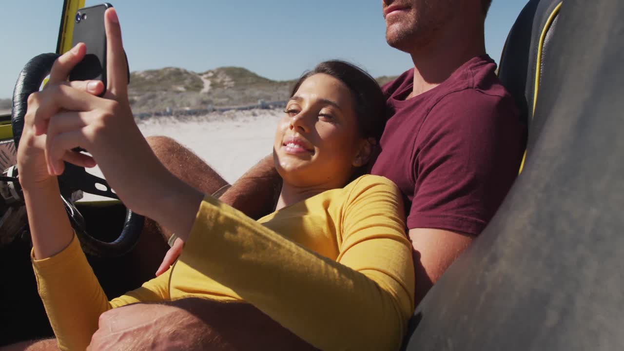 feliz pareja caucásica sentada en un buggy de playa junto al mar hablando