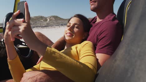 Happy-caucasian-couple-sitting-in-beach-buggy-by-the-sea-talking