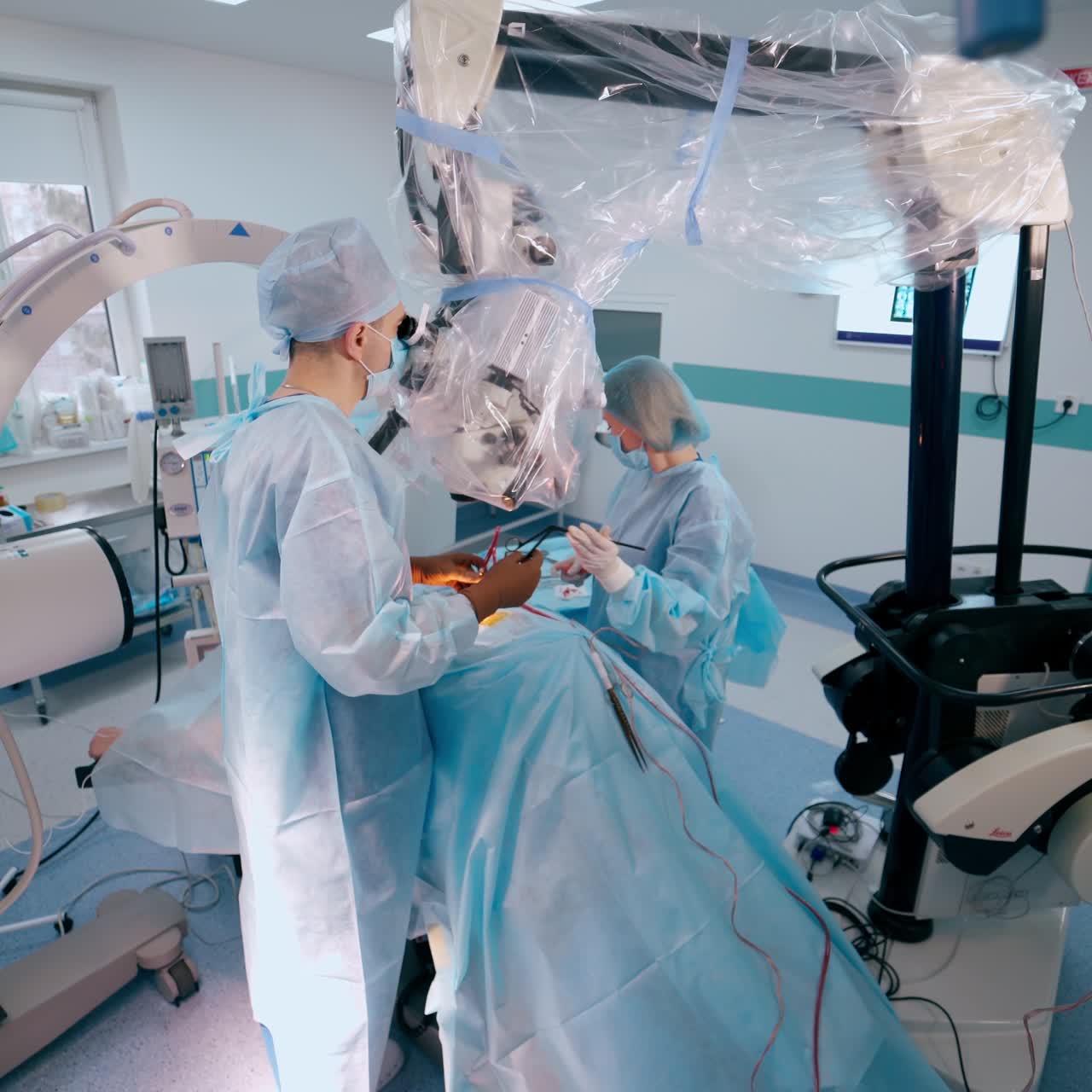 Professional doctor and female assistant performing a surgery looking through the microscope. Nurse assists a professional surgeon in the modern operating room.