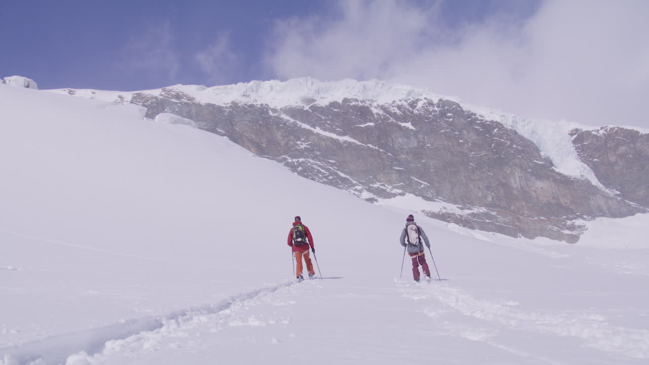 Due freerider salgono con lo sci alpinismo sul maestoso Alphubel con la loro guida, poi scendono attraverso un terreno glaciale circondato da crepacci e seracchi nel paesaggio alpino d'alta quota di Saas-Fee