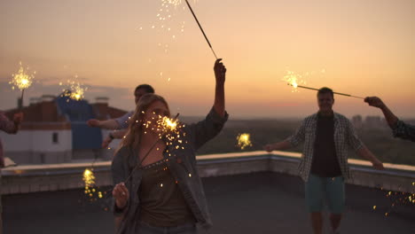 Young-girls-on-the-roof-move-a-dance-with-her-friends-on-a-summer-evening-with-big-bengal-light.-It's-a-pleasure-sunset-before-night.-Their-hair-blows-beautifully-in-the-wind.