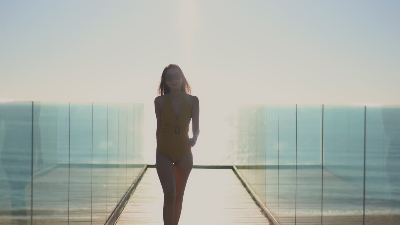 Donna giovane e in forma che cammina in controluce e al rallentatore mentre percorre il sentiero che conduce al bordo della piscina del resort