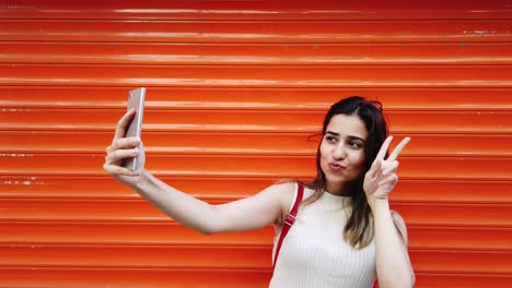 Zeitlupe:-Schönes-Junges-Mädchen-Macht-Selfie-Mit-Smartphone-Vor-Orangefarbenem,-Rotem-Hintergrund