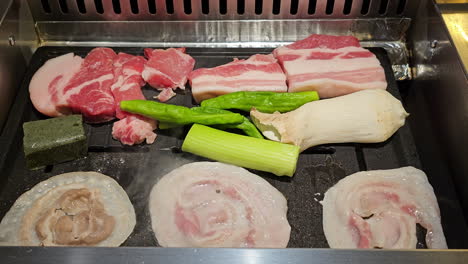 Korean-BBQ---Slices-of-raw-pork-belly-with-visible-layers-of-fat-and-meat-fried-on-a-grill-with-mushrooms-and-green-onion-at-Restaurant--closeup