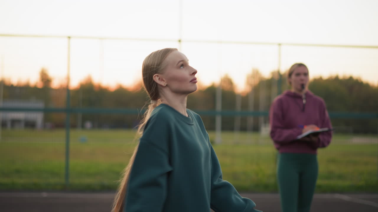 principiante de voleibol siendo observado por el entrenador durante el servicio, libro de rendimiento en la mano, silbido en la boca, técnica de monitoreo en el exterior