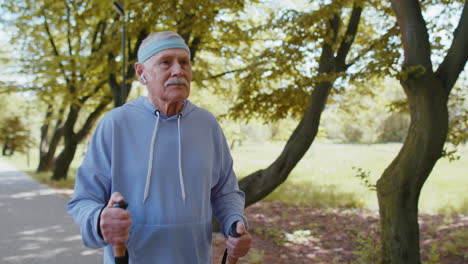 Elderly-pensioner-old-man-grandfather-training-Nordic-walking-use-ski-trekking-poles-in-summer-park