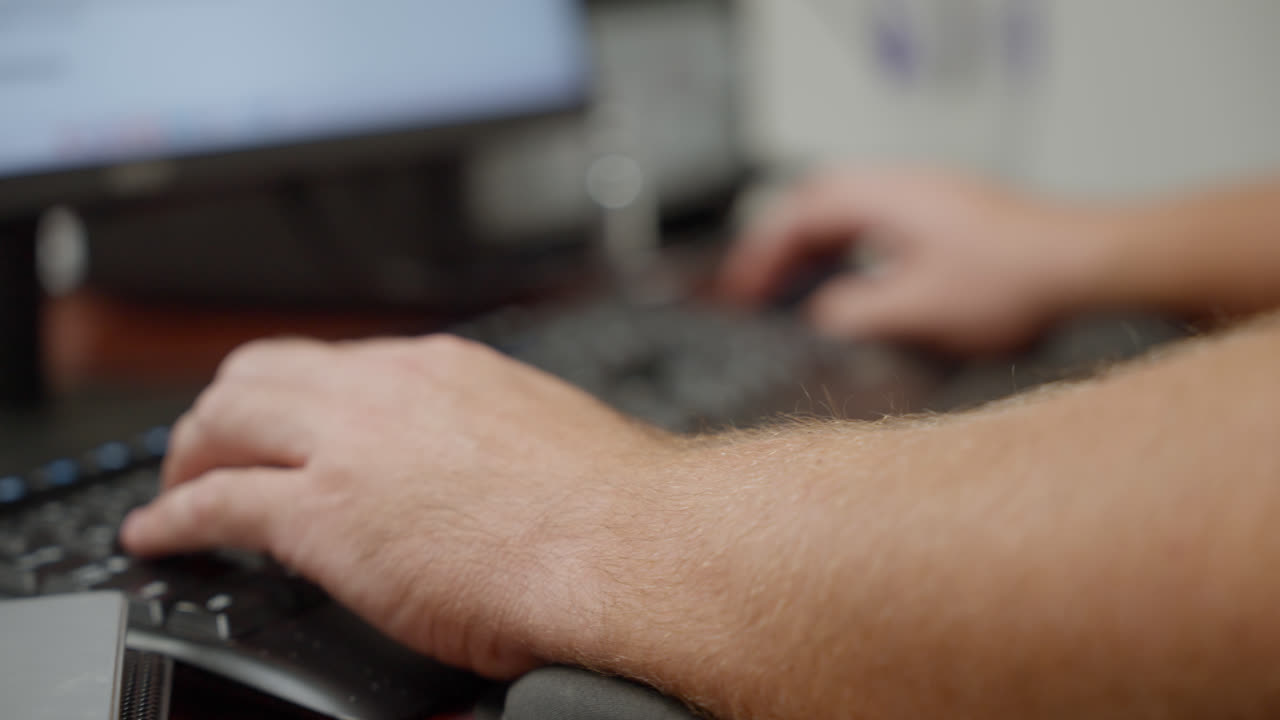 A slow orbit extreme close up around hands typing on a keyboard at a computer workstation