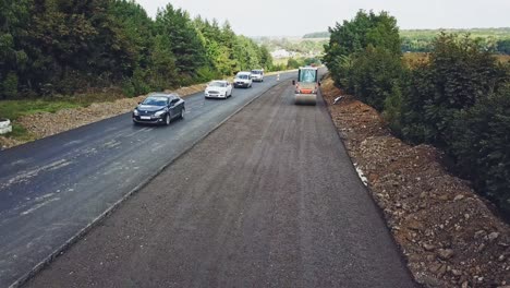vibratory roller compresses fresh asphalt on one side of the road on the background of the movement of cars on the other side of the road. modern equipment for road construction works. aerial view.