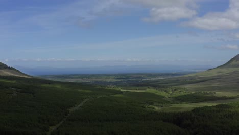 gleniff horseshoe valley, sligo, ireland, june 2021. drone looking north with donegal mountains on the horizon while slowly pulling backwards over rugged fields and woodlands.
