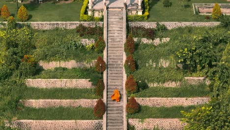 mujer con vestido de gasa naranja subiendo empinados escalones en el parque ujung, templo de bali