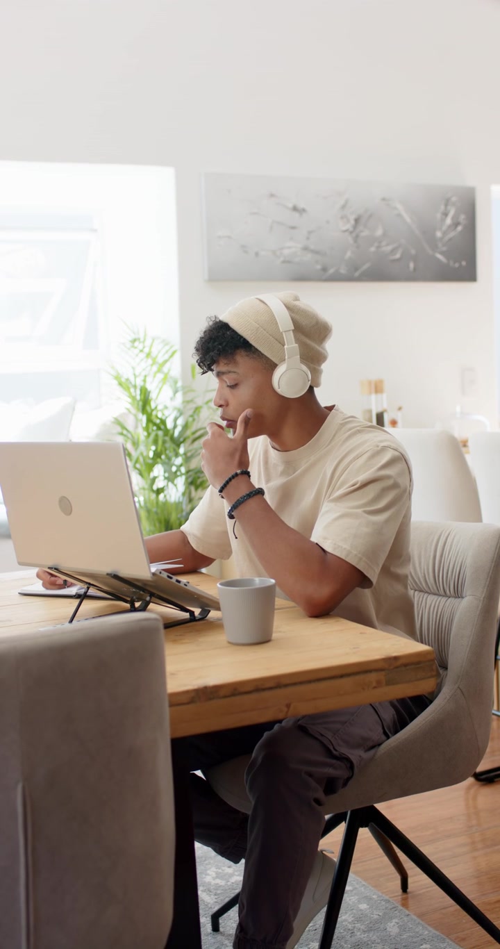 Vertical video: African American man adjusting headphones, using tablet and laptop for work