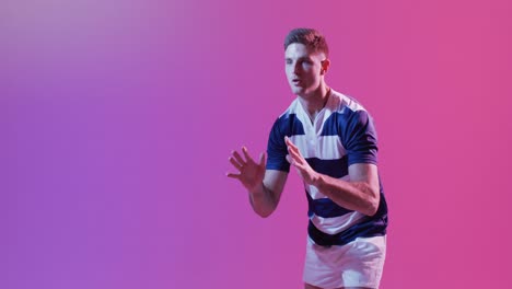 Caucasian-male-rugby-player-catching-rugby-ball-over-pink-lighting