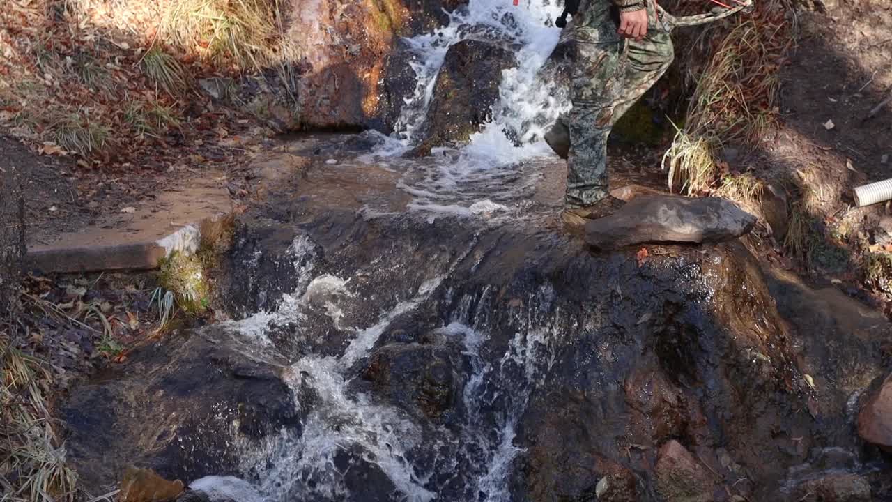 Slow motion shot of a hunter walking across a mountain stream in Utah