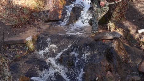 slow motion shot of a hunter walking across a mountain stream in utah