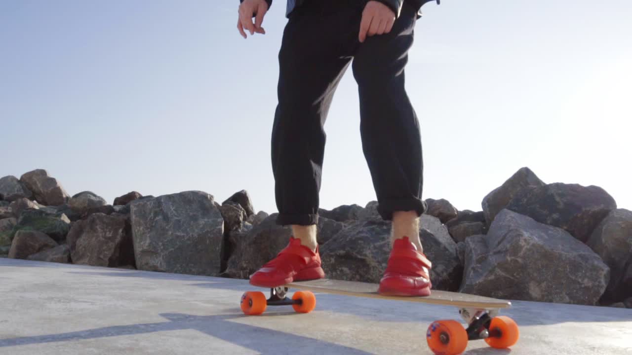 Young man in red sneakers skates by the sea