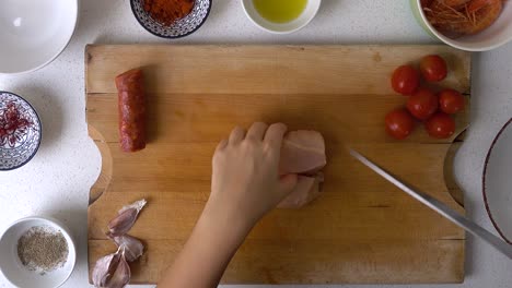 looking down on hands of male chef, cutting chicken on wooden cutting board