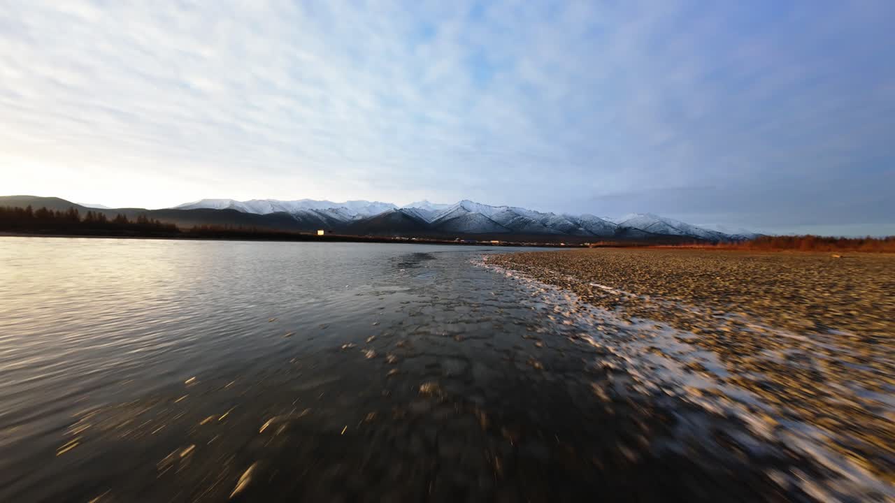 Experience the breathtaking beauty of Yakutia as the drone glides over serene waters and majestic mountains at dawn, revealing nature's tranquil charm in this remote region.