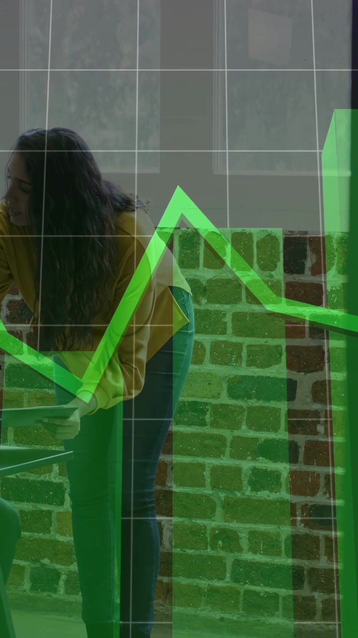 Vertical video: Woman reaching tablet and showing data to peer, green charts animating over tablet