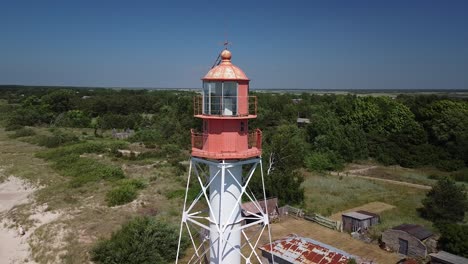 Hermosa-Vista-Aérea-Del-Faro-De-Acero-Pintado-De-Blanco-Con-La-Parte-Superior-Roja-Ubicada-En-Pape,-Letonia-En-La-Costa-Del-Mar-Báltico-En-Un-Día-Soleado-De-Verano,-órbita-De-Disparo-De-Drones-De-Gran-Angular-A-La-Izquierda