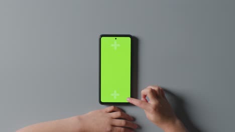 overhead studio shot of child scrolling on green screen mobile phone