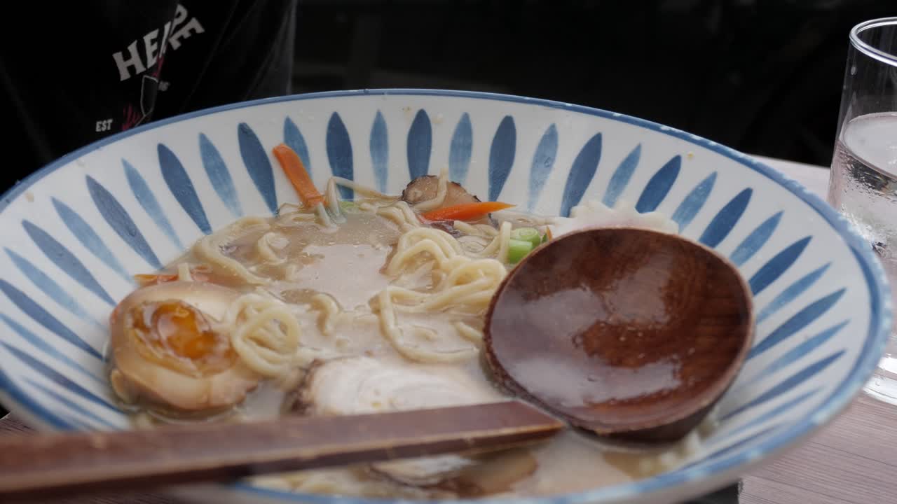 A person using chopsticks to enjoy a warm bowl of Tonkotsu ramen with char siu pork