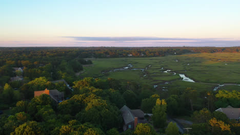 cape cod bay aerial drone footage of houses, marsh, tall green grass and water creeks at golden hour surrounded by trees