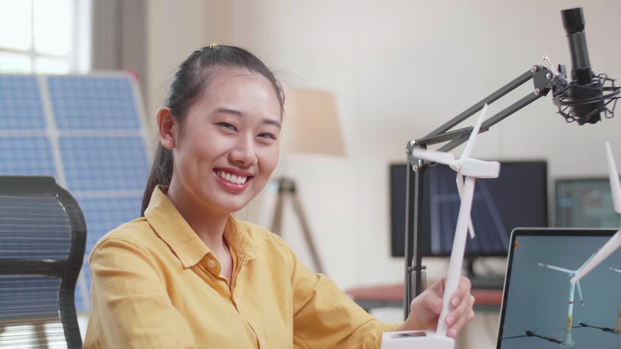 아시아 여성이 사무실에서 태양전지 에 노트북으로 작업하는 동안 풍력 터빈을 보고 카메라에 미소 짓고 있습니다.