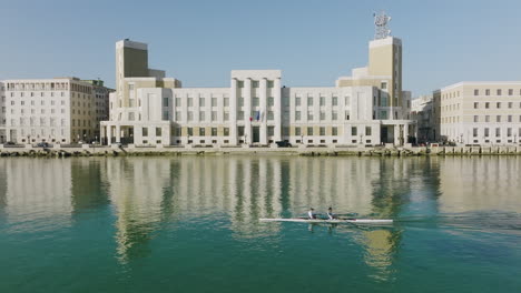 a team of rowers going by a municipal building in bari, italy in the early morning