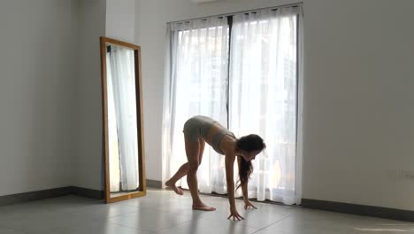 mujer practicando yoga matutino en una habitación iluminada por el sol, estirándose con una expresión serena, espejo a un lado