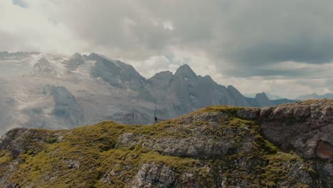 parallax aerial shot of a explorer walking on top of a mountain ridge, revealing a glacier on the top of the steep mountains in the background, cinematic grade