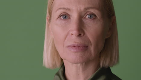 Close-Up-View-Of-Blonde-Mature-Woman-With-Blue-Eyes-Smiling-At-Camera-On-Green-Background